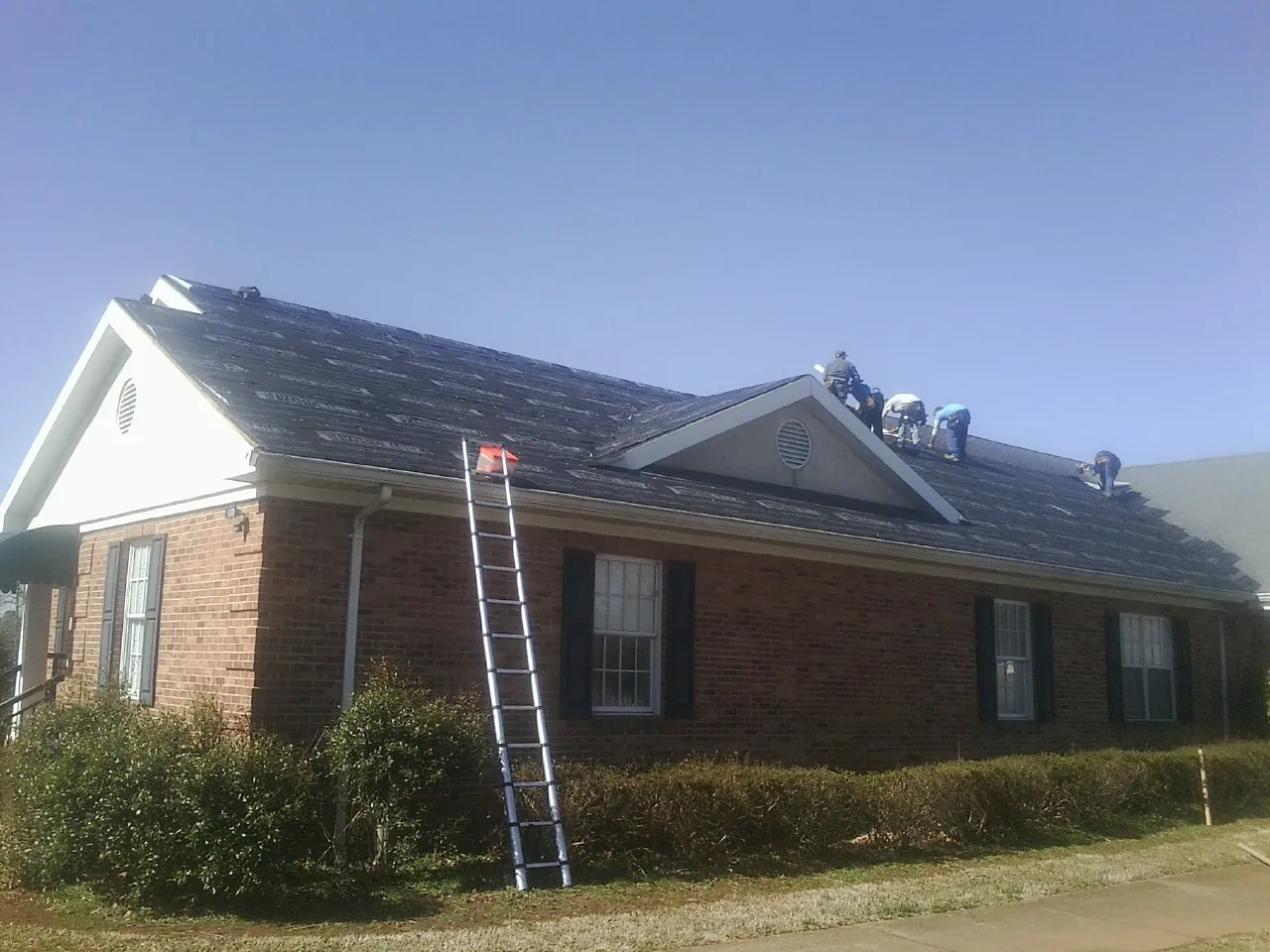 Crew tearing shingles off a brick ranch roof with a ladder set — Metal Roof Repair work by our crew in Big Rock