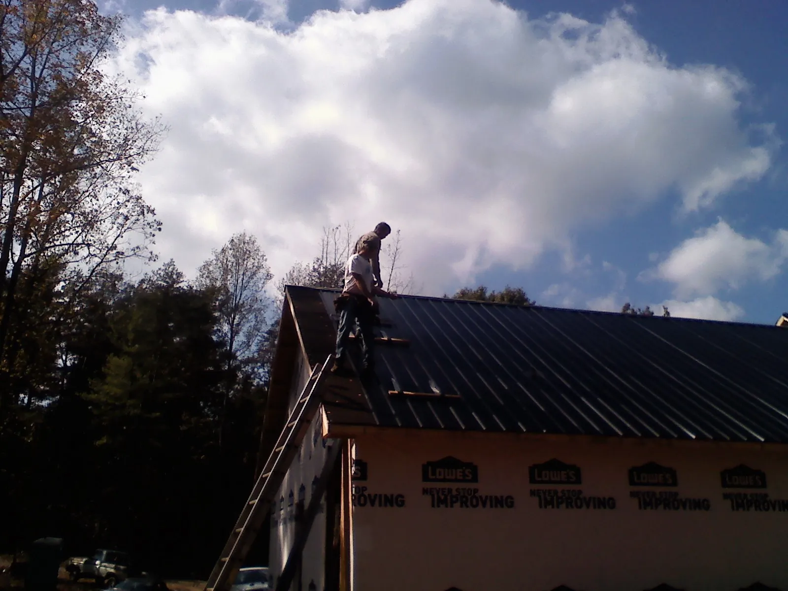 Roofer fastening dark metal panels high against a cloudy sky, from a Roof Inspection job in Big Rock