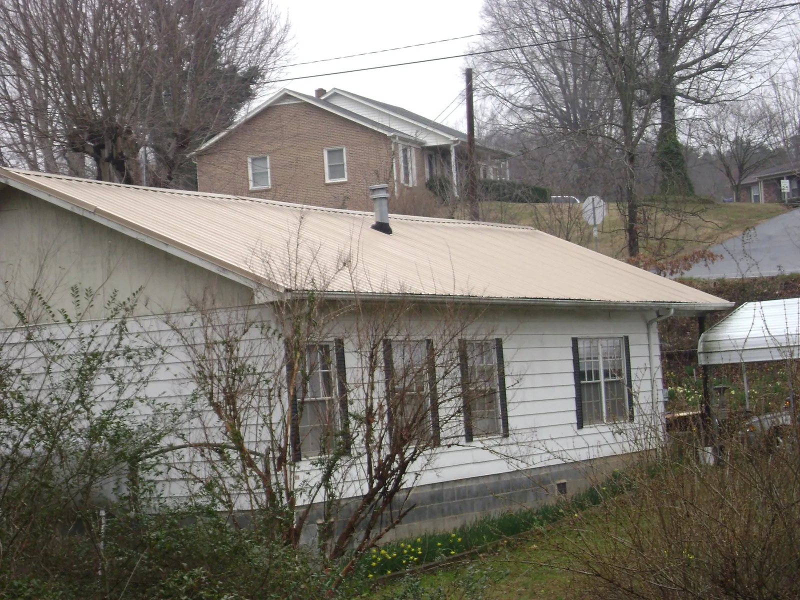 Tan metal roof on a white sided house set into a hillside — Commercial Roofing by Roofing Brothers in Big Rock